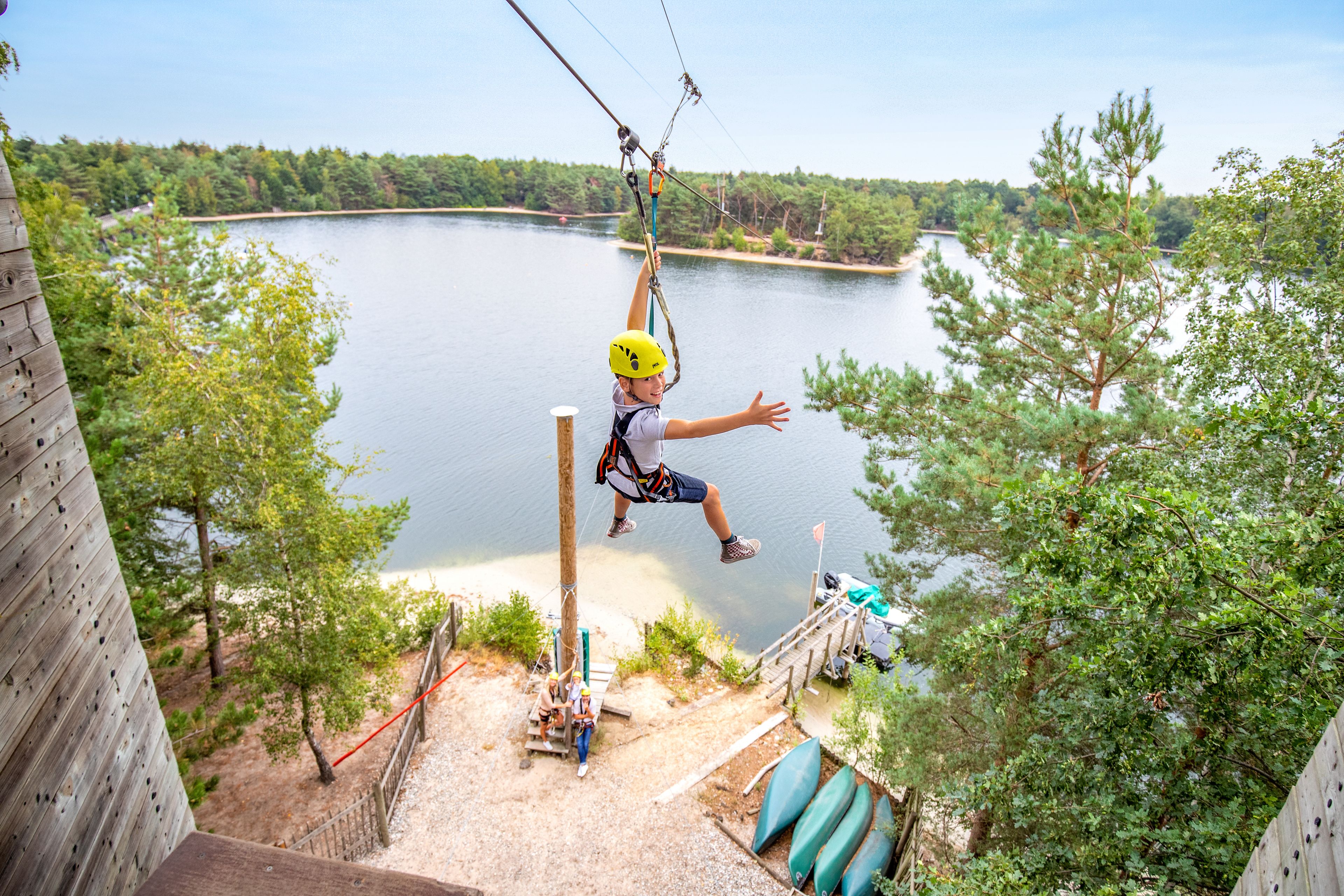 A person zip-lining over a lake with a wooden platform and trees in the background.