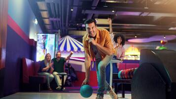 A bowling alley with a person in an orange shirt preparing to bowl. There are seating areas with people watching.