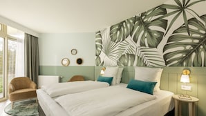 Une chambre d’hôtel avec un grand lit, deux tables de chevet, une chaise et un mur décoré d’un motif de feuilles tropicales.