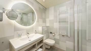 Une salle de bain moderne avec un grand miroir rond, un lavabo blanc, des toilettes et une douche en verre.