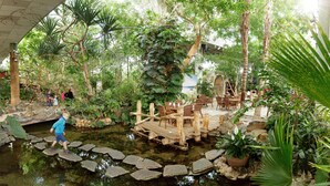 Un jardin intérieur doté d’un bassin, d’un pont en bois et d’un espace détente entouré d’une végétation luxuriante.