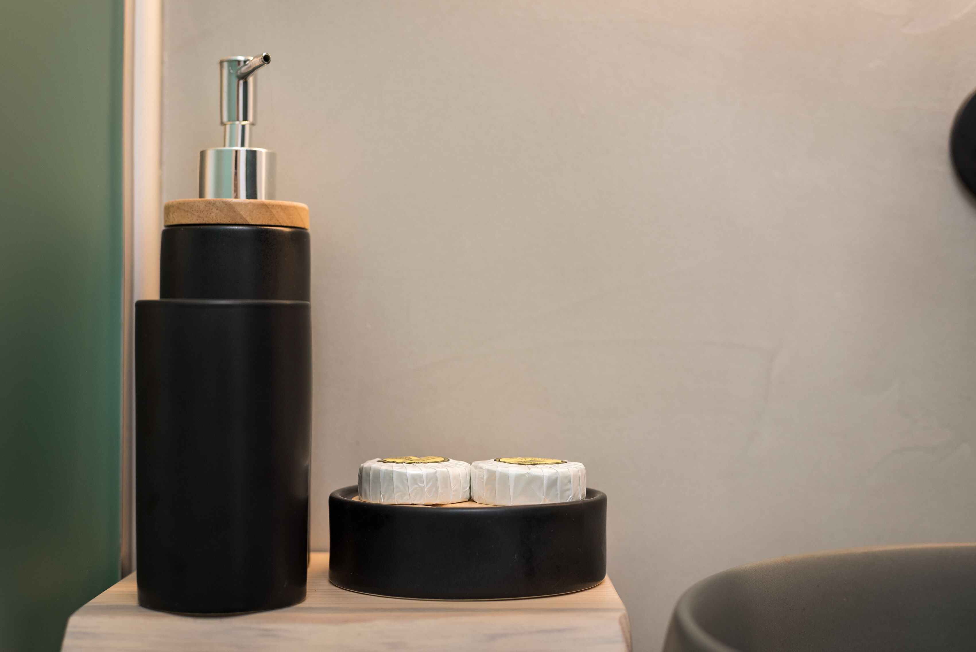 Un objeto cilíndrico negro con una bomba en la parte superior, un recipiente negro más pequeño con dos objetos blancos, y una pared verde.