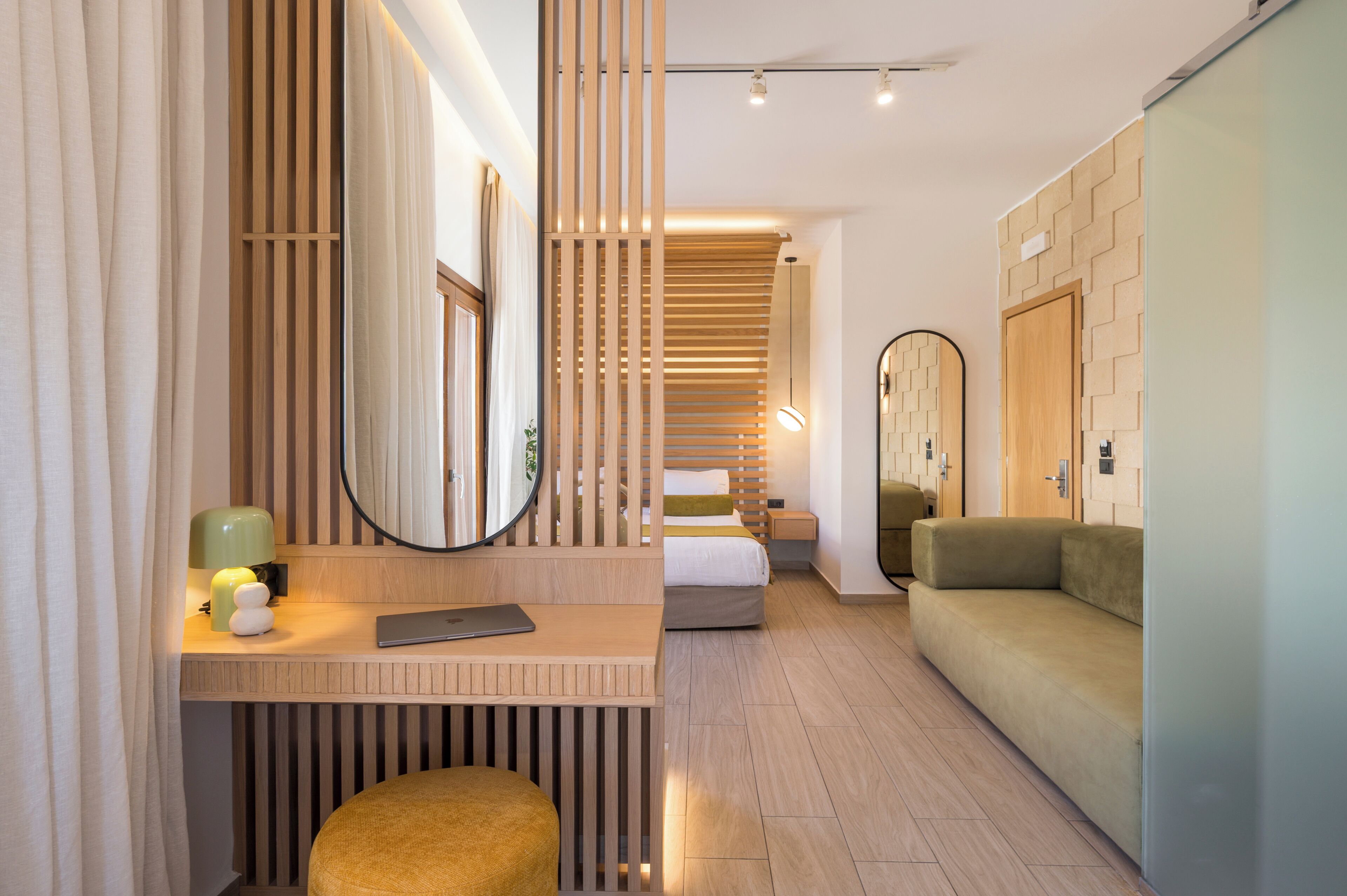 Una habitación de hotel moderna con un escritorio de madera, una cama, un sofá y un espejo grande.