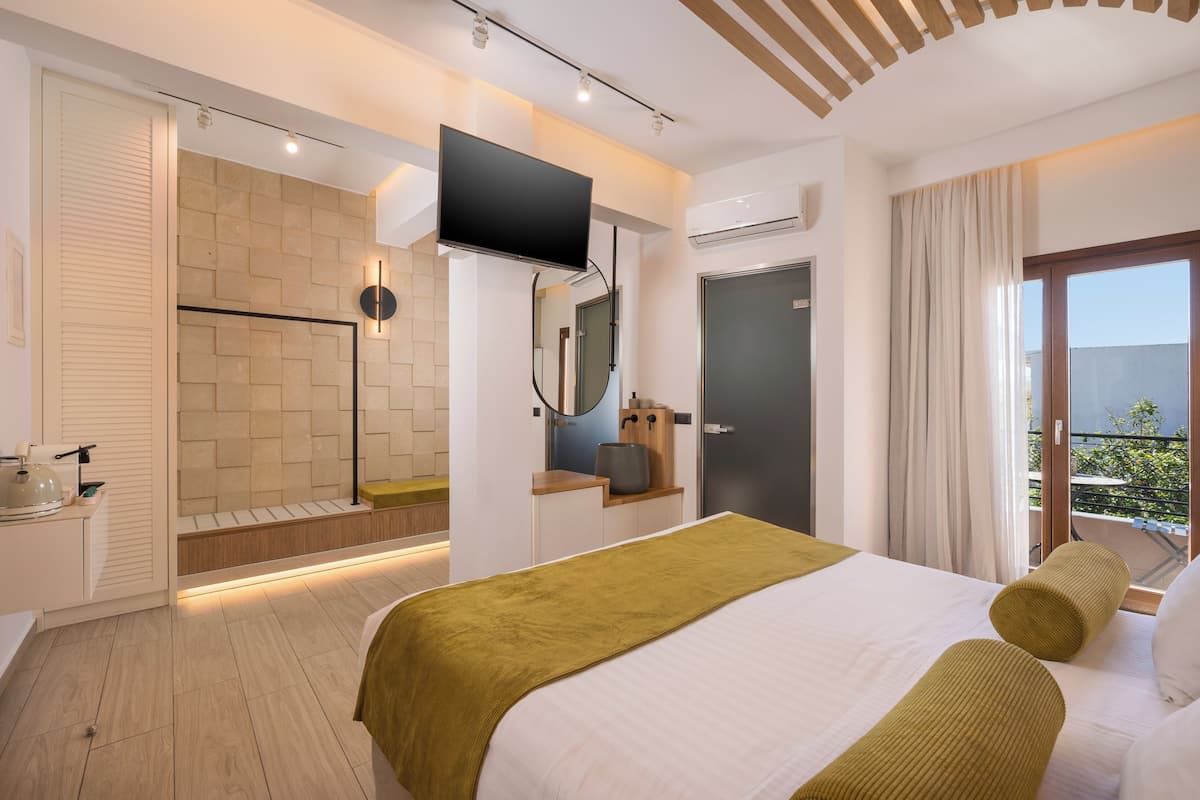 Una habitación de hotel moderna con una cama grande, un televisor de pantalla plana sobre la cama, un vestidor y un balcón con vistas.