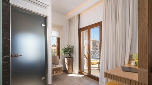 Ein modernes Hotelzimmer mit einer Schiebeglasdoor zum Balkon, einem hölzernen Schreibtisch mit Laptop, einer großen Topfpflanze und einem bequemen Sessel.
