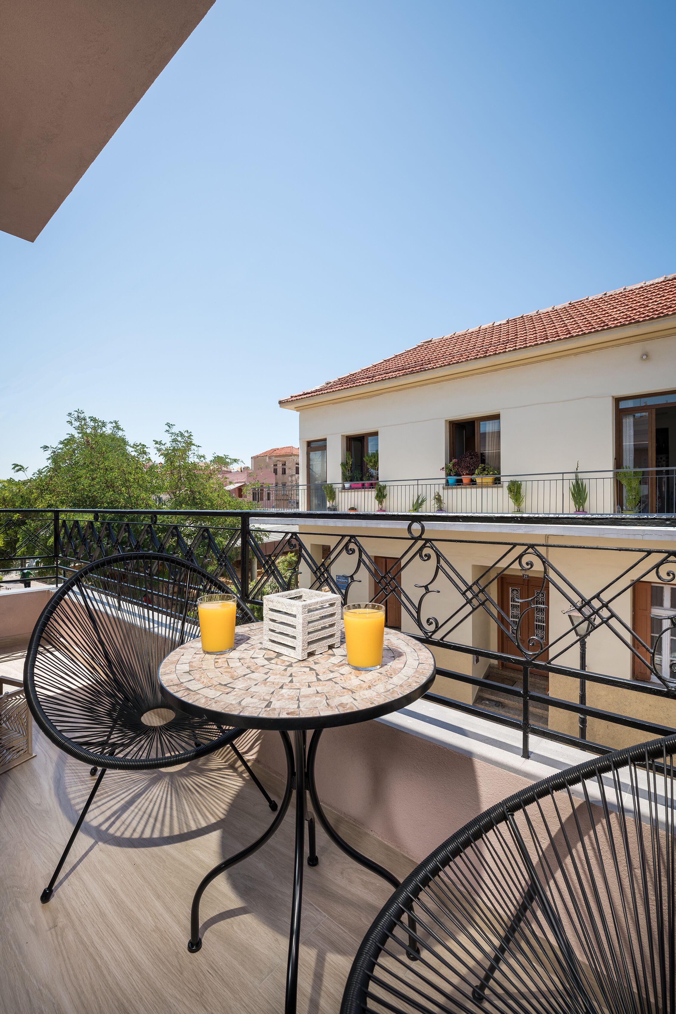 A balcony with a round table, two chairs, and two glasses of orange juice.