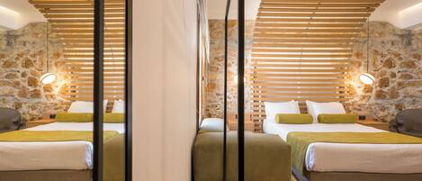 A hotel room with two beds, wooden slatted headboards, stone walls, and a modern light fixture.