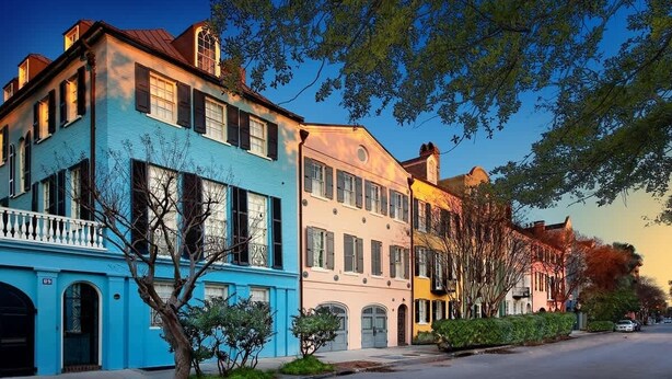 A row of colorful townhouses with balconies, a clear sky, and a tree-lined street.