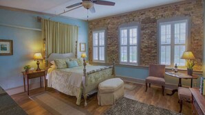 A bedroom with a bed, bedside tables, a chair, a table, and a window with shutters.