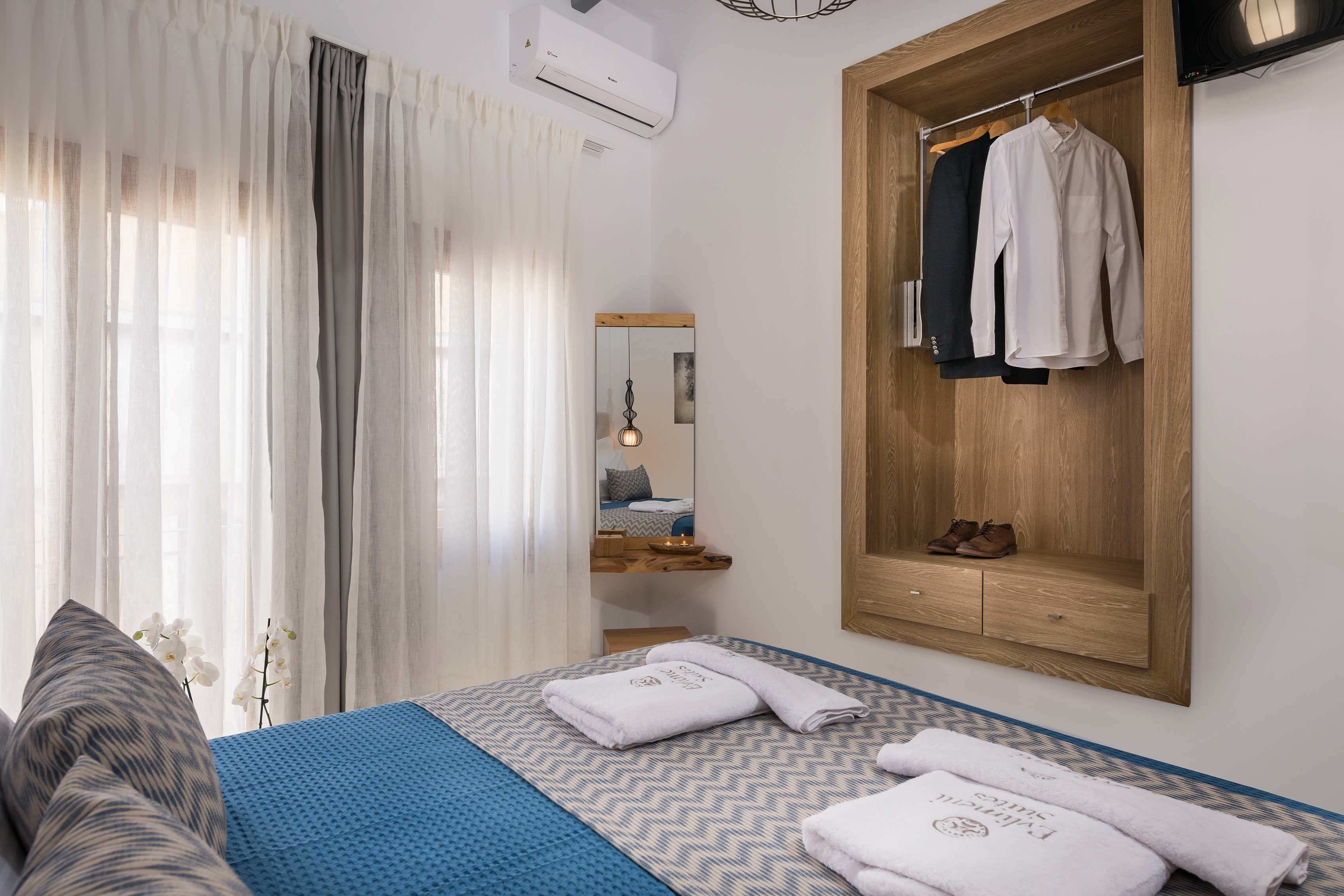 A bedroom with a bed, a wooden wardrobe, a mirror, and a hanging light fixture.