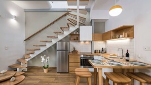 A modern kitchen with wooden stairs, a dining area with stools, and a built-in oven. - Evlimeni Suites (Chania)