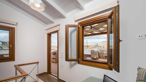 A room with a wooden desk, a laptop, a window with a view of buildings, and a staircase. - Evlimeni Suites (Chania)