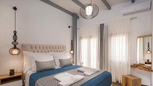 A neatly arranged bedroom with a large bed, bedside tables, a mirror, and a hanging light fixture. - Evlimeni Suites (Chania)
