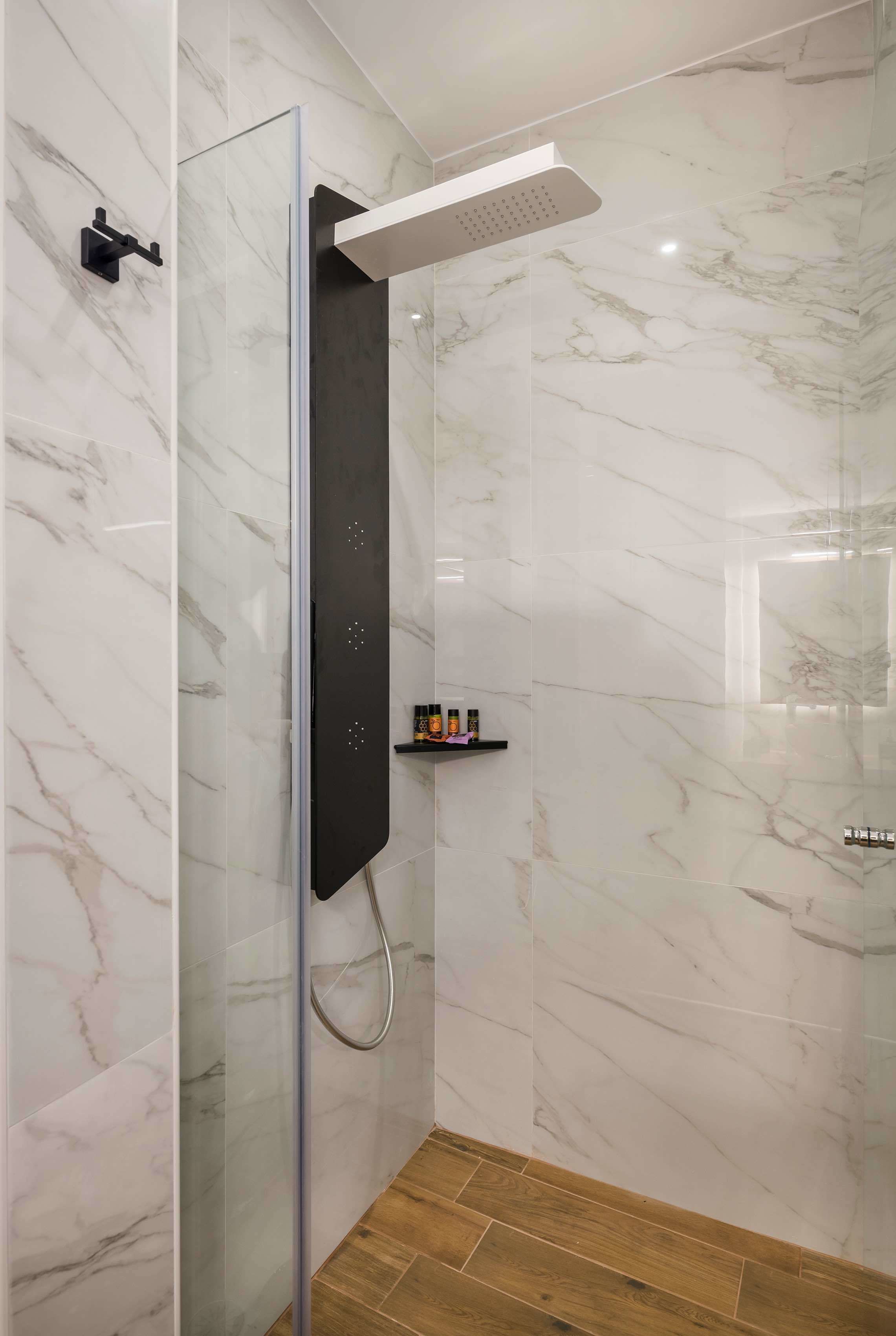 Un espace douche moderne doté d’une paroi en verre, de murs en marbre et d’un plancher en bois.
