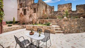 An outdoor patio with stone flooring, a table with chairs, and a bottle of wine. - Evlimeni Suites (Chania)