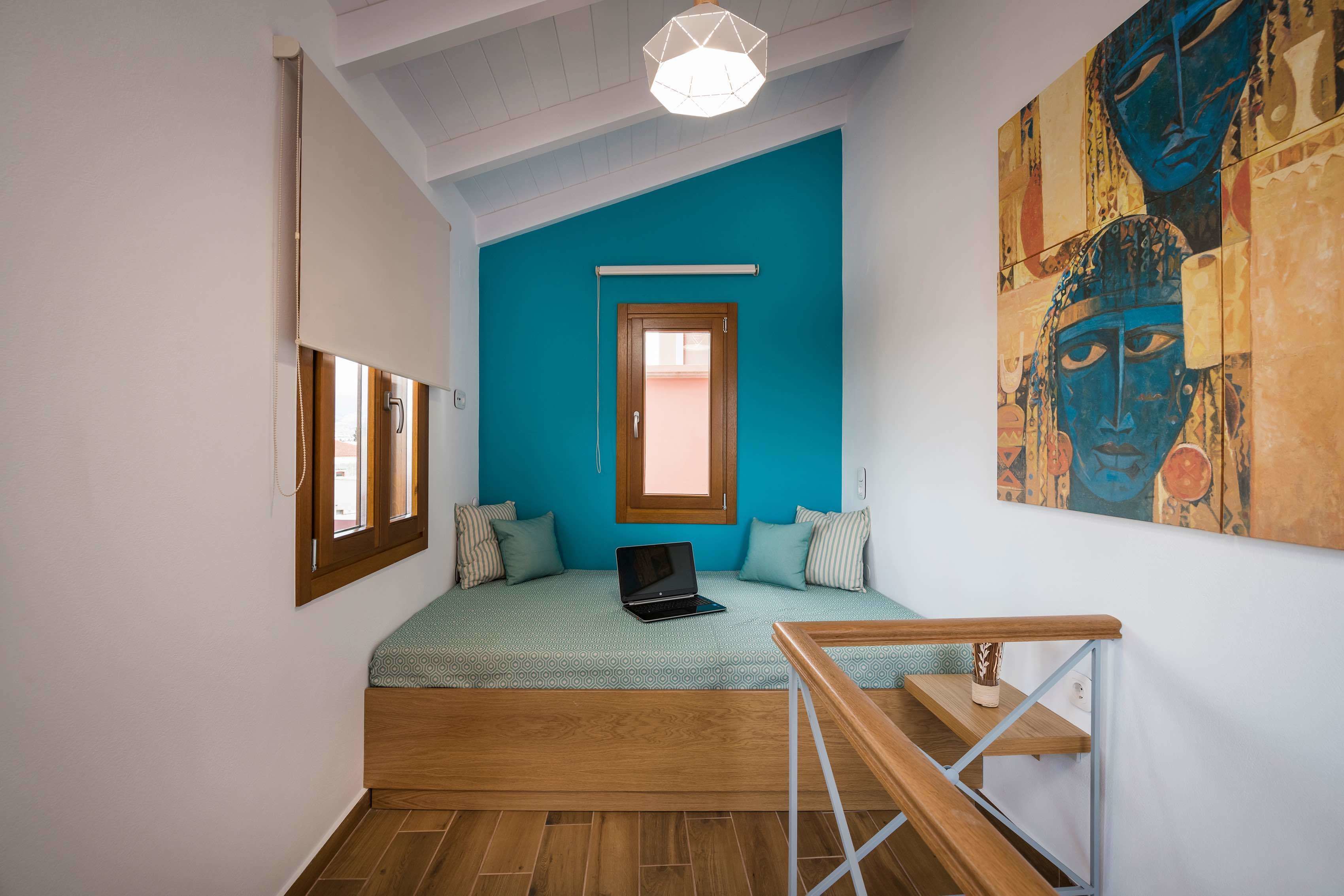 A room with a bed, a laptop on the bed, a window, a painting on the wall, and a staircase.
