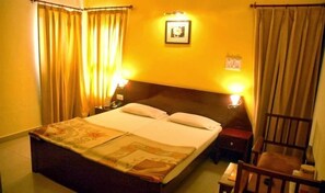 A hotel room with a large bed, two bedside tables, a chair, and curtains. - Hotel Grace (Gwalior)