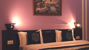 A bedroom with a bed, two bedside lamps, a painting on the wall, and a nightstand with a lamp. - Hotel Grace (Gwalior)