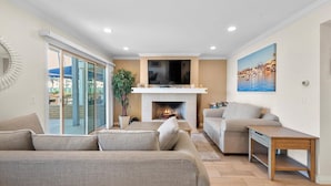 A modern living room with a fireplace, a television, and a painting of a coastal scene. - Oceanfront Boardwalk property, Newly remodeled Large patio, Steps to the sand. (Newport Beach)