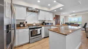 A modern kitchen with white cabinets, a granite countertop, stainless steel appliances, and a large island. - Oceanfront Boardwalk property, Newly remodeled Large patio, Steps to the sand. (Newport Beach)