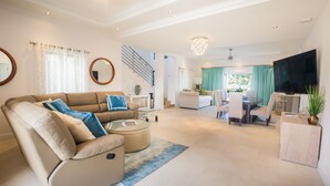 Een ruime woonkamer met een bank, salontafel en een televisie. Er is een trap die naar een ander niveau leidt.