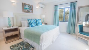 Een slaapkamer met een bed, nachtkastjes, een stoel, een raam met gordijnen en een schilderij aan de muur.