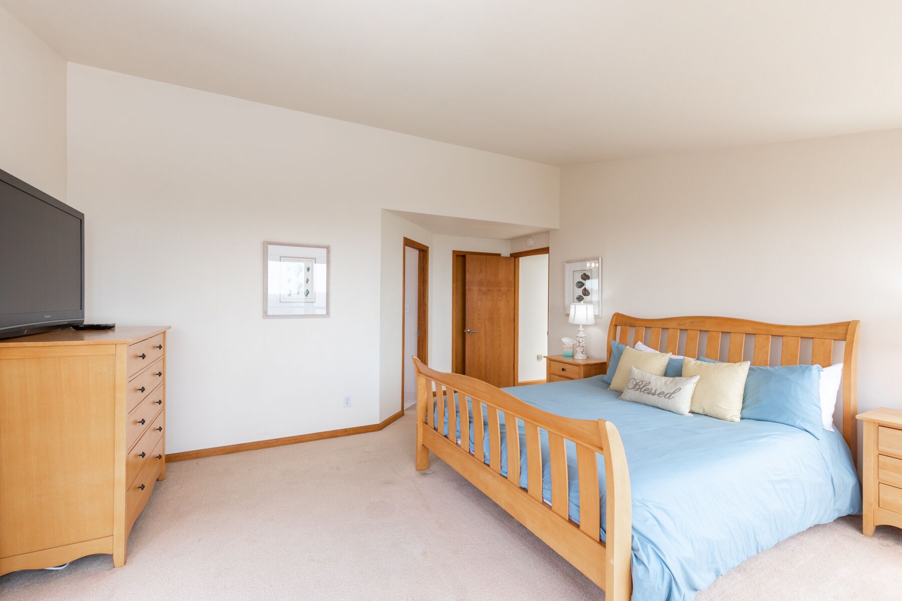 A bedroom with a wooden bed, a television on a wooden dresser, and a framed picture on the wall.