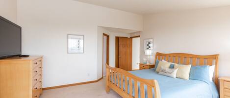 A bedroom with a wooden bed, a television on a wooden dresser, and a framed picture on the wall.