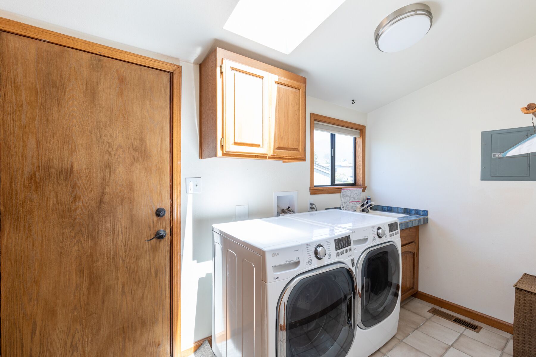 A laundry room with a front-loading washer and dryer, wooden cabinets, a window, and a skylight.