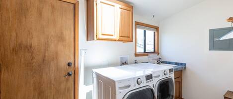 A laundry room with a front-loading washer and dryer, wooden cabinets, a window, and a skylight.