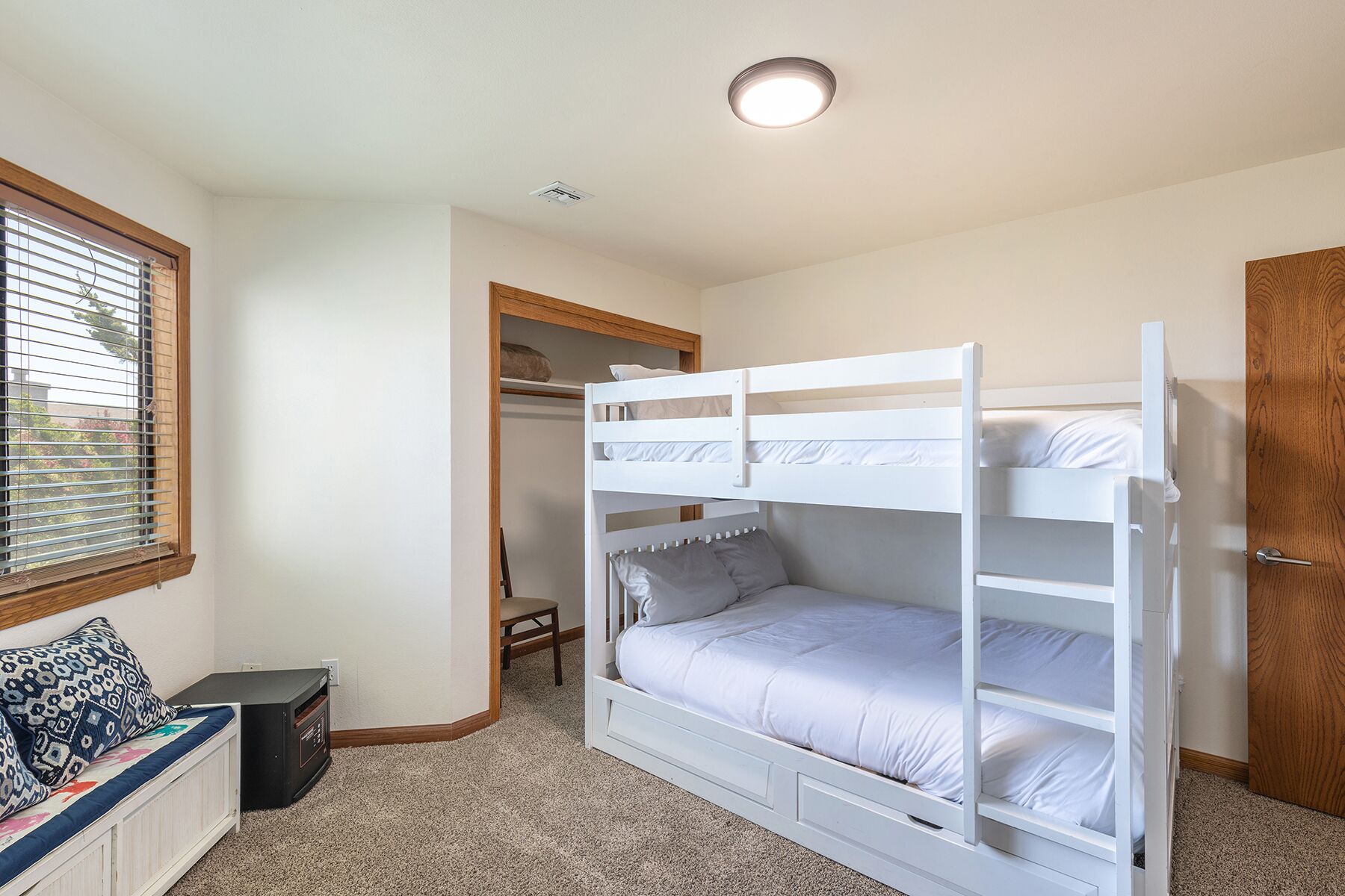 Une chambre avec un lit superposé, une fenêtre, un bureau et une armoire.