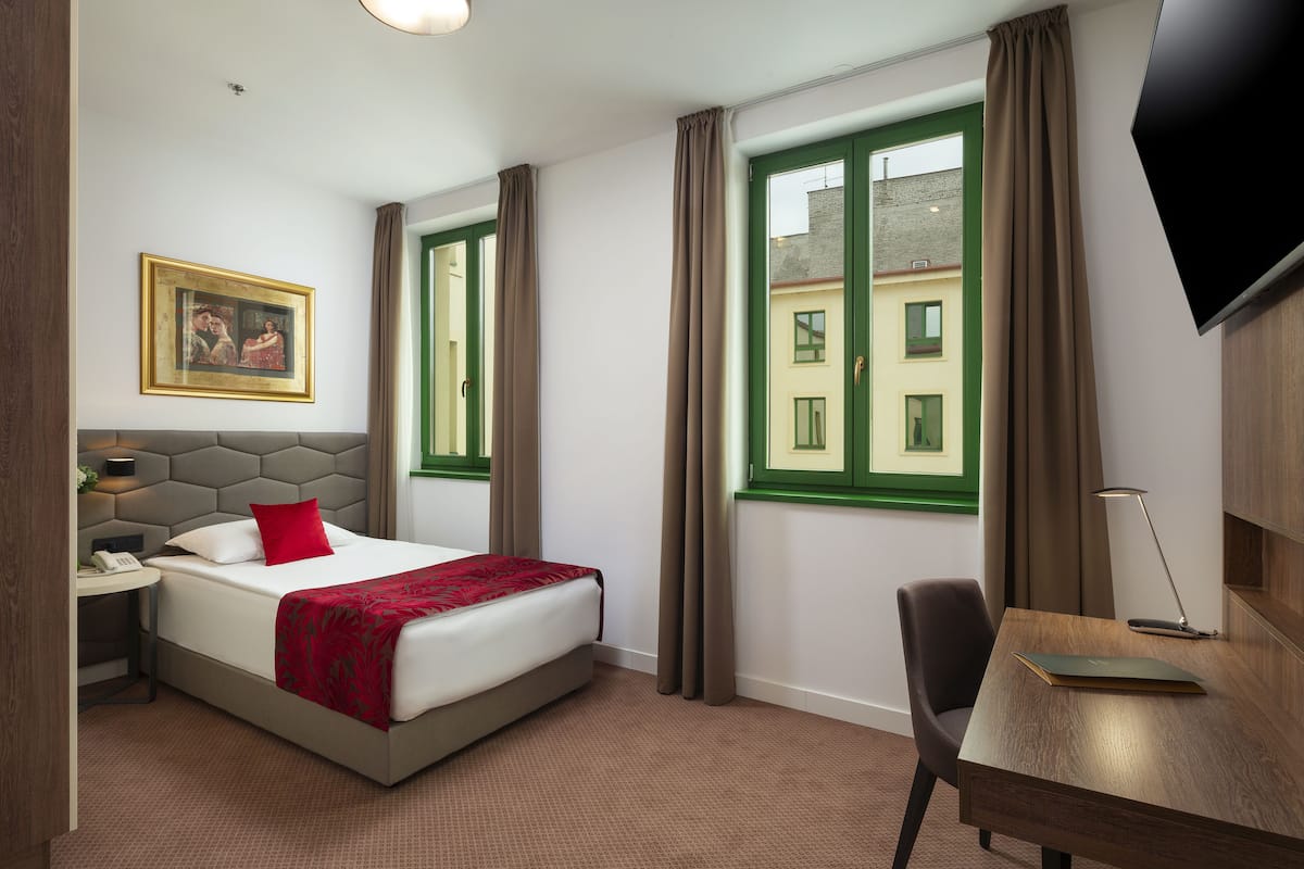 Ein Hotelzimmer mit Bett, Schreibtisch, Stuhl, Fernseher, einem Gemälde und einem Fenster mit Vorhängen.