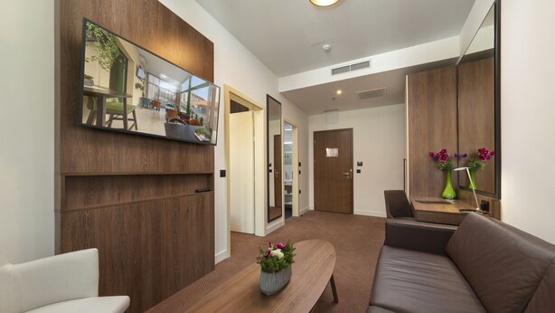 A modern hotel lobby with a wooden reception desk, a brown leather sofa, and a large mirror reflecting the interior. - Hotel Park 45 (Zagreb)
