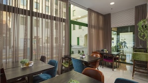 A dining area with wooden tables and chairs, potted plants, and a view of the street outside. - Hotel Park 45 (Zagreb)