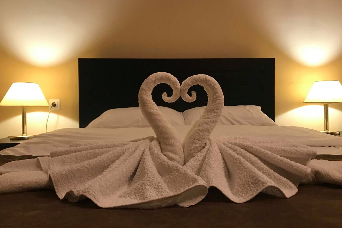 Ein Hotelzimmer mit einem Bett, zwei Nachttischlampen und einer herzförmigen Handtuchgestaltung auf dem Bett.