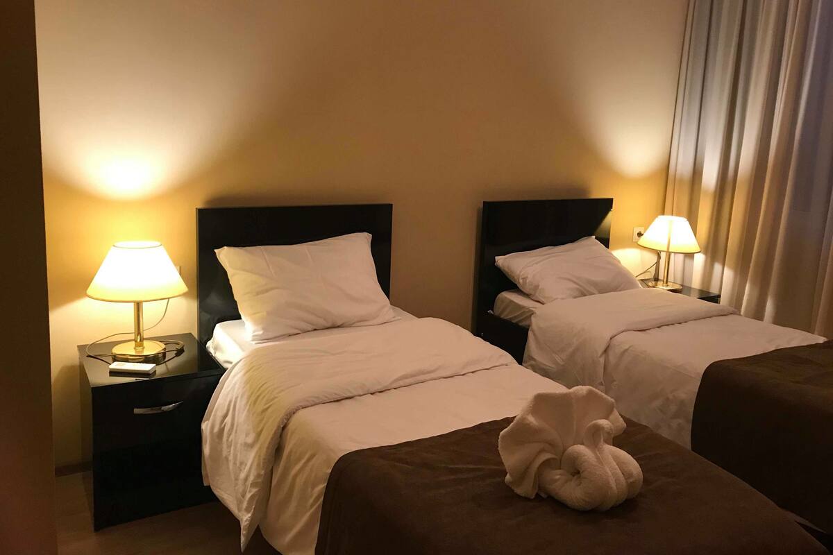 Ein Hotelzimmer mit zwei Betten, jeweils mit Kissen und einer Lampe auf einem Nachttisch.