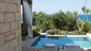 A pool area with two lounge chairs, a stone wall, and a view of the sea. - Pantanassa Villas (Chania)