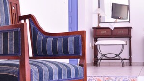 A wooden chair with a blue and white patterned cushion, a blue door, a wooden dresser with a mirror, and a tiled floor with floral patterns. - Villa Notos (Milos)