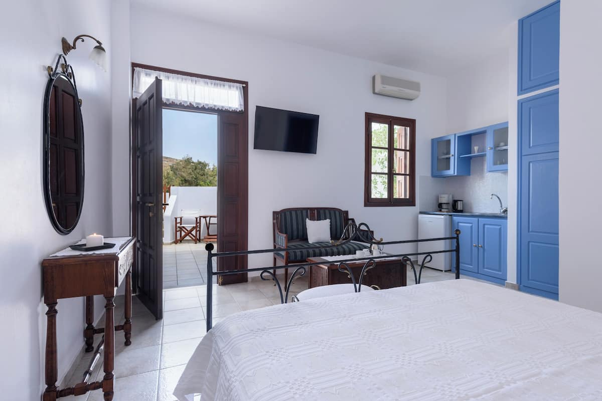 Un dormitorio con cama, escritorio, silla, televisor, ventana y puerta que da a un espacio exterior.
