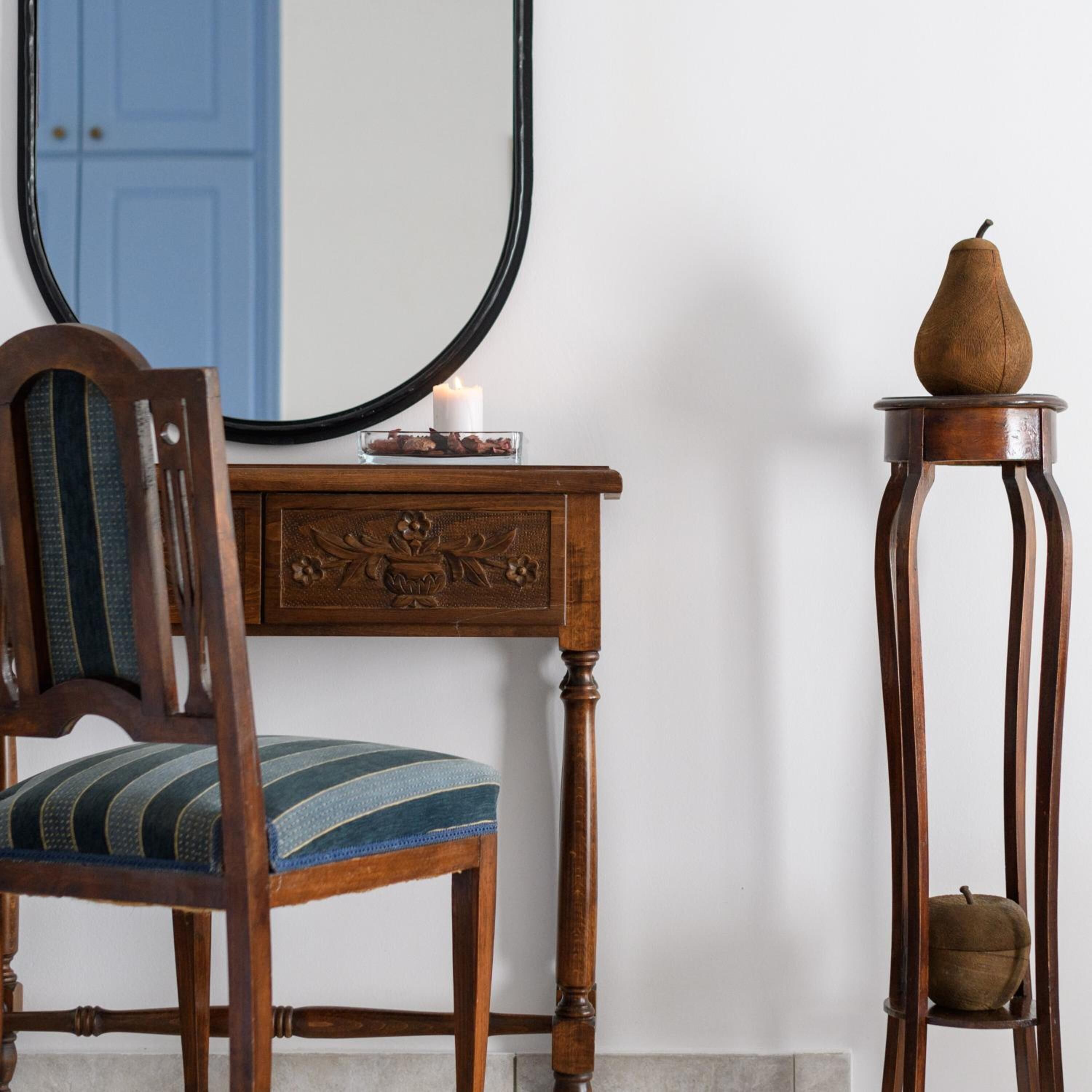 A wooden chair with a striped cushion, a wooden dresser with a mirror, and a small table with a pear on top.