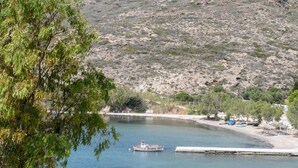 A small boat on calm water, surrounded by sparse vegetation and a hilly landscape. - Villa Notos (Milos)