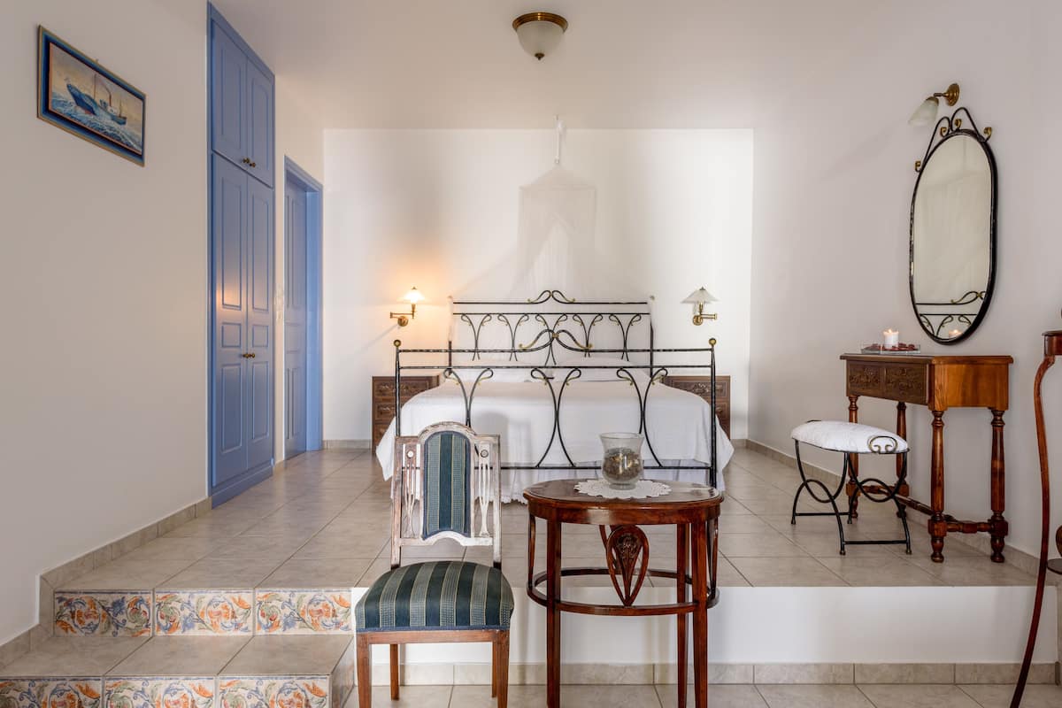 Un dormitorio con cama, mesitas de noche, una silla, una pequeña mesa y un espejo.