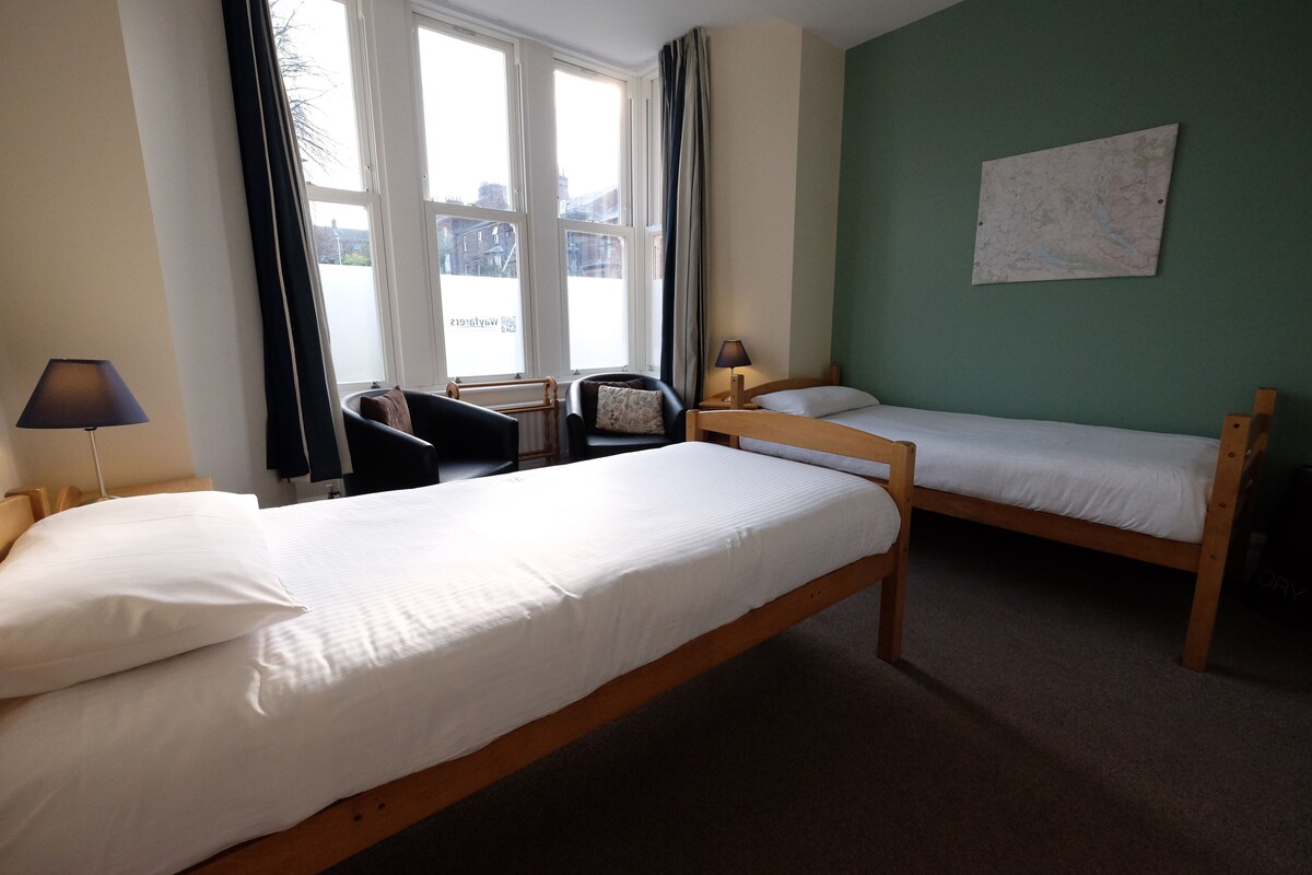 A room with two wooden beds, a chair, a desk, and a window with curtains.