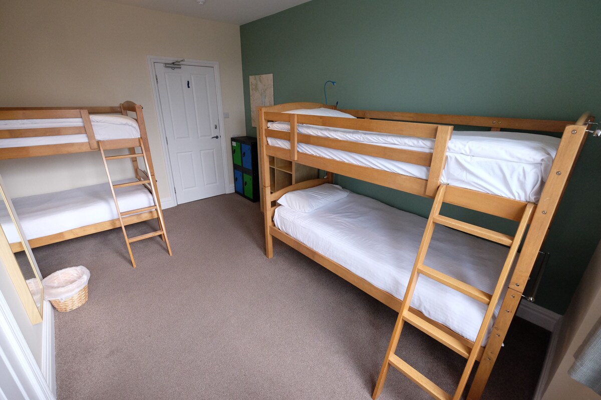 A room with two bunk beds, a door, a wall-mounted shelf, and a carpeted floor.