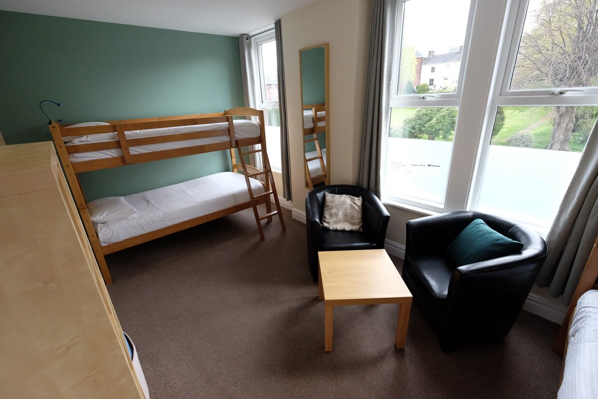 A room with bunk beds, a small table, a chair, and a window with a view of the outside.
