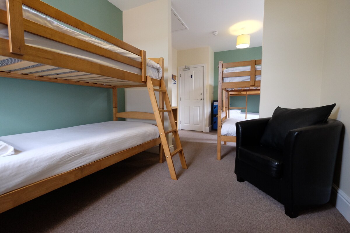 A bunk bed room with a ladder, a black chair, and a door in the background.