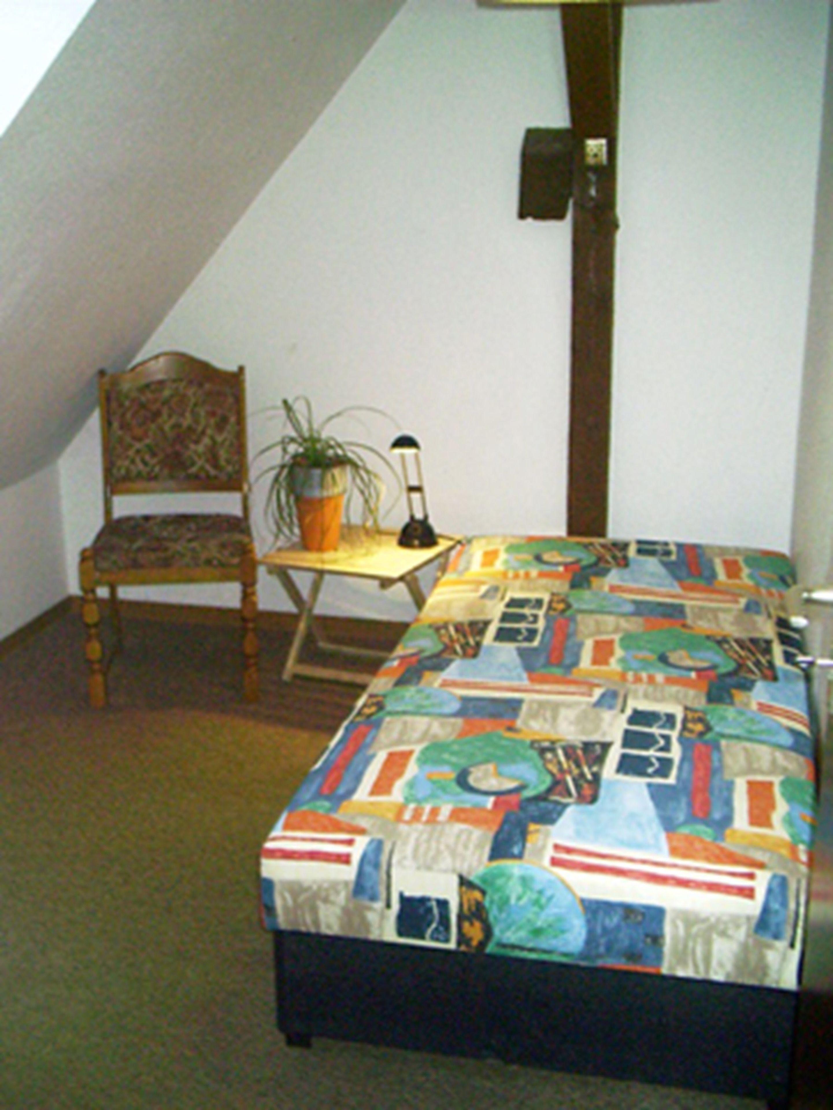 A small, cozy room with a bed, a chair, a table, and a lamp.