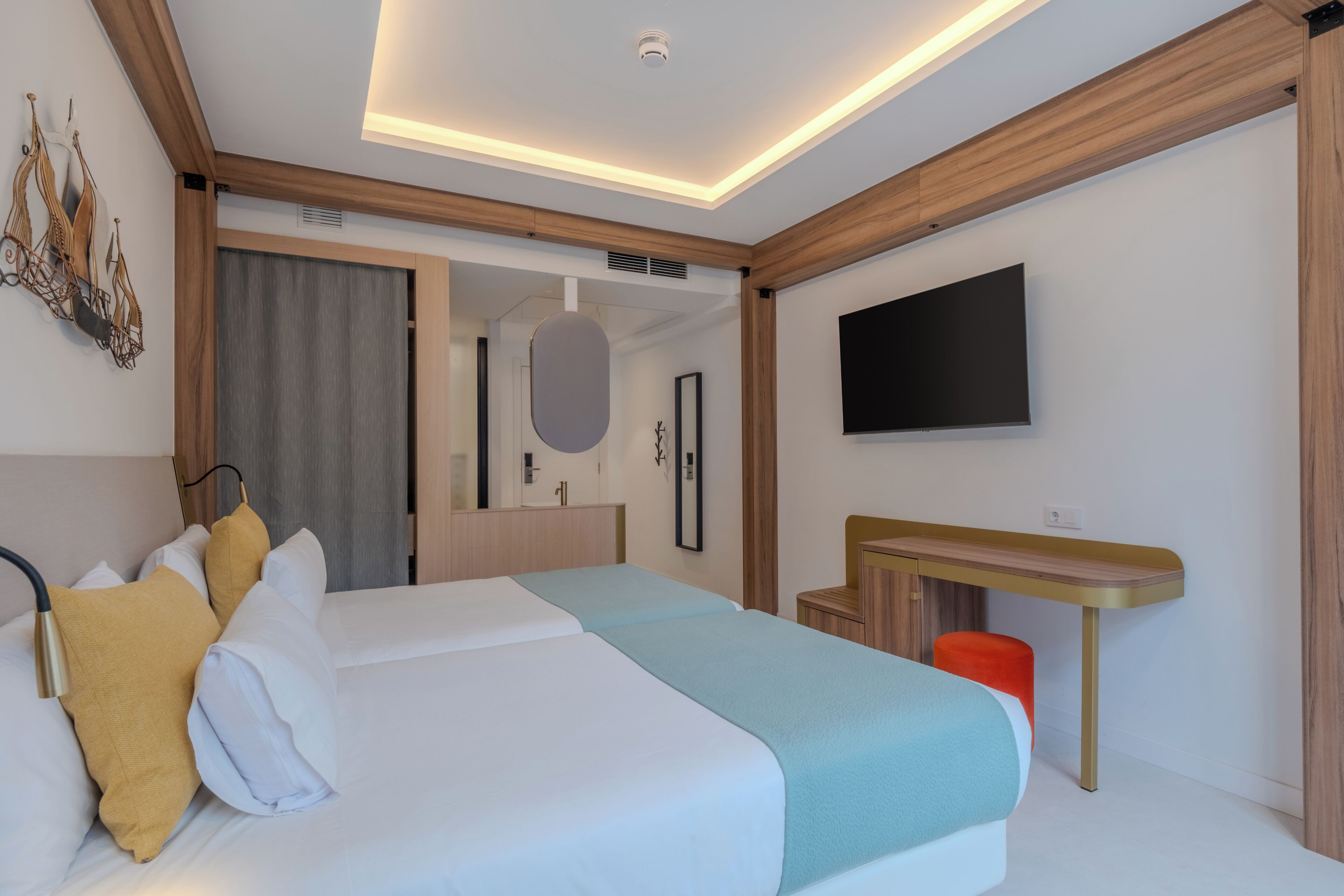 A modern hotel room with a large bed, a desk, a flat-screen TV, and a large mirror.