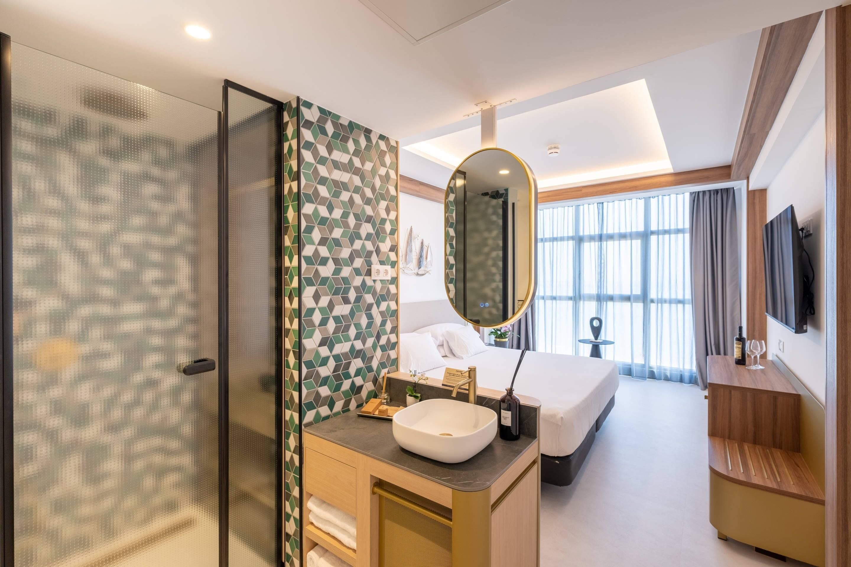 A hotel room with a large bed, a bathroom with a mirror and sink, and a TV on the wall.