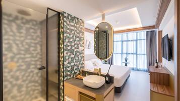 A hotel room with a large bed, a bathroom with a mirror and sink, and a TV on the wall.